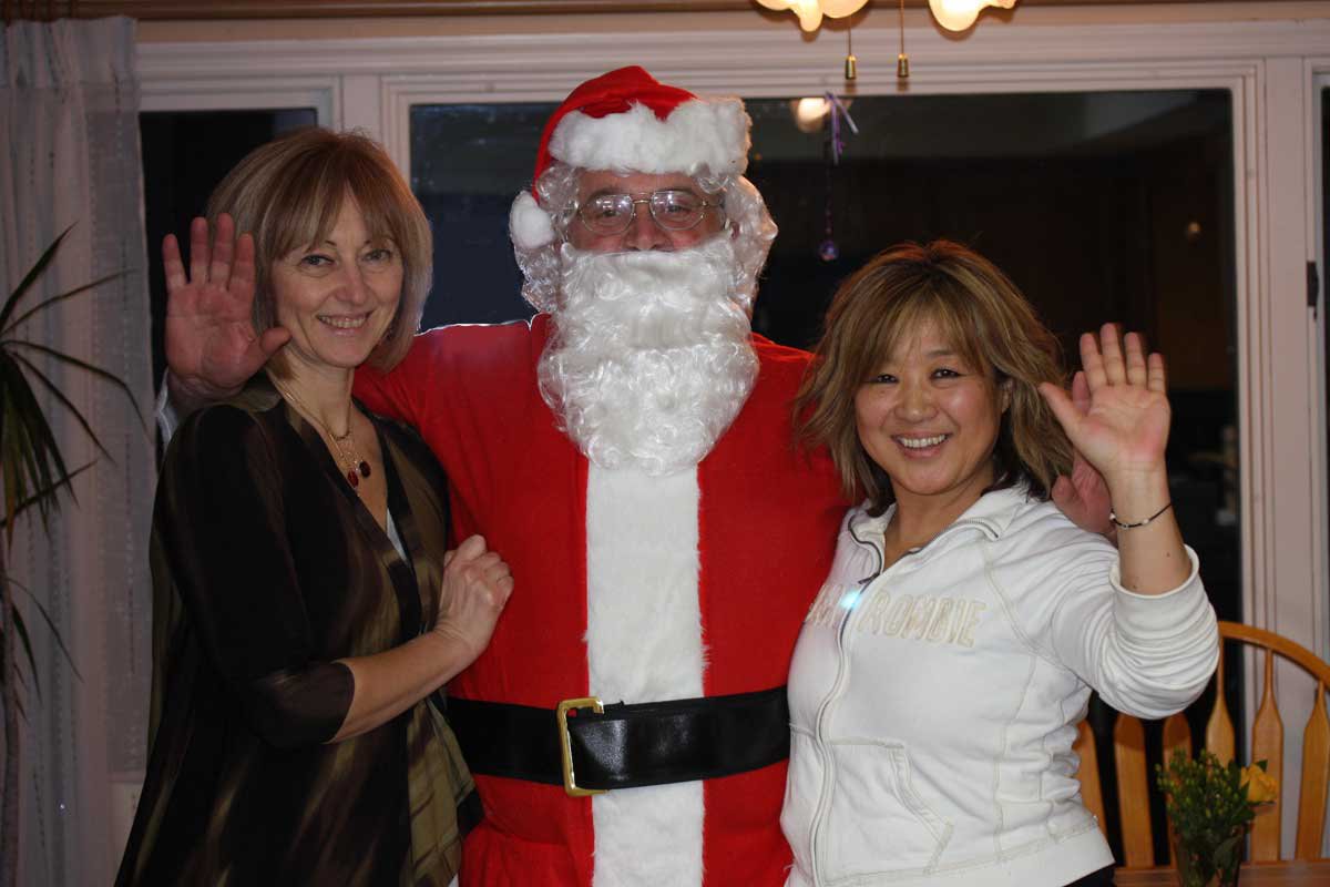 A person in a santa garment with two women wavingAI-generated content may be incorrect.